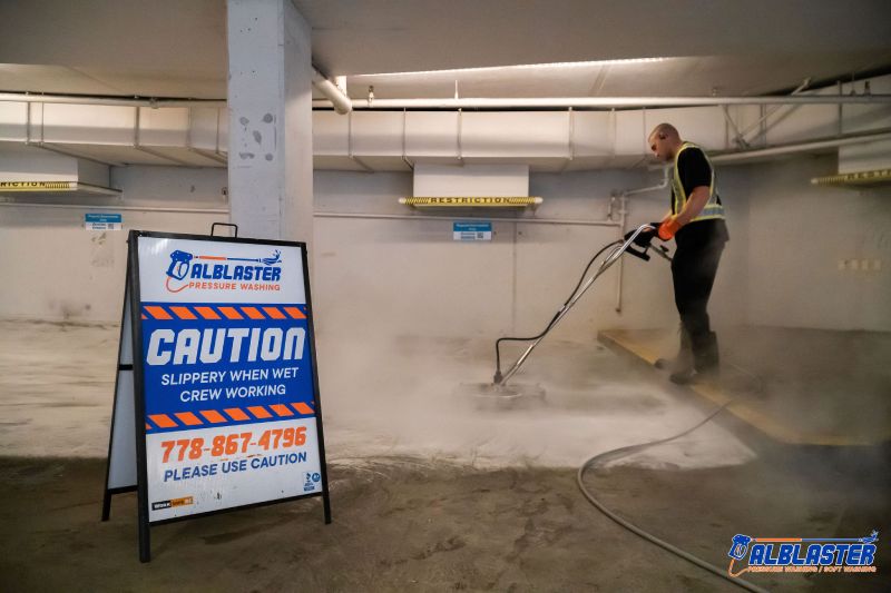 Technician is performing pressure washing service in an underground parking lot in front of Alblaster commercial board