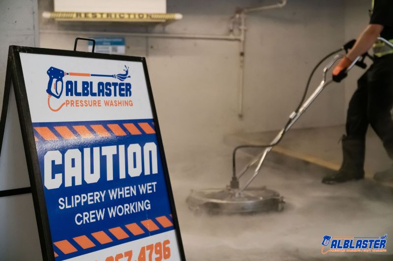 Technician is performing pressure washing service in an underground parking lot in front of Alblaster commercial board