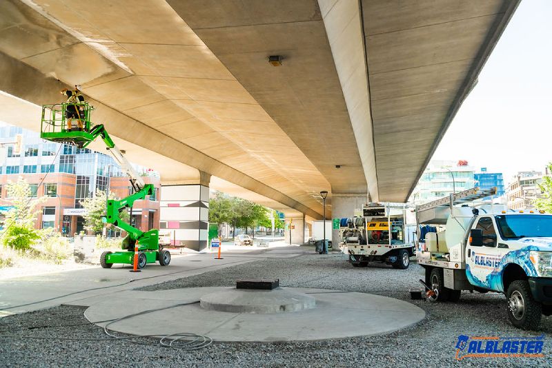 A contractor is performing pressure washing on a ladder under Cambie Bridge in Vancouver